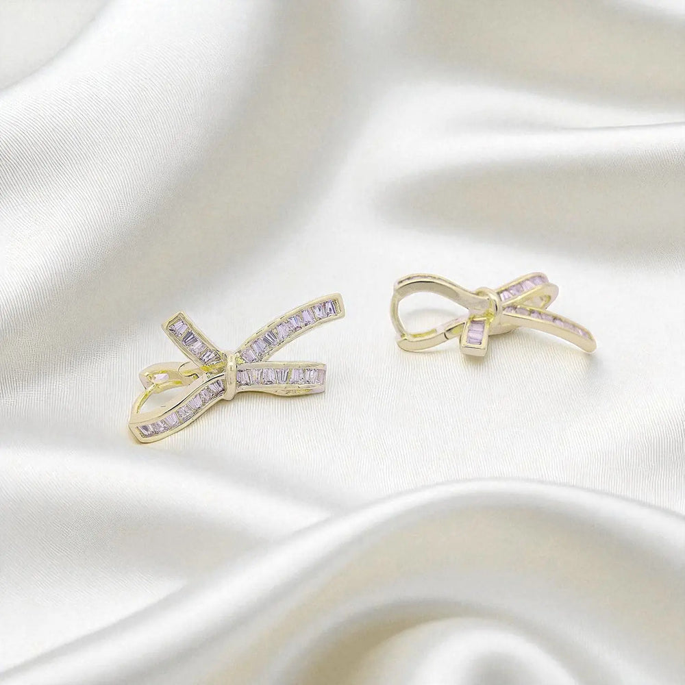 
                      
                        Goudkleurige strik oorbellen met trapezium zirkonia stenen  Victoria Valenza
                      
                    